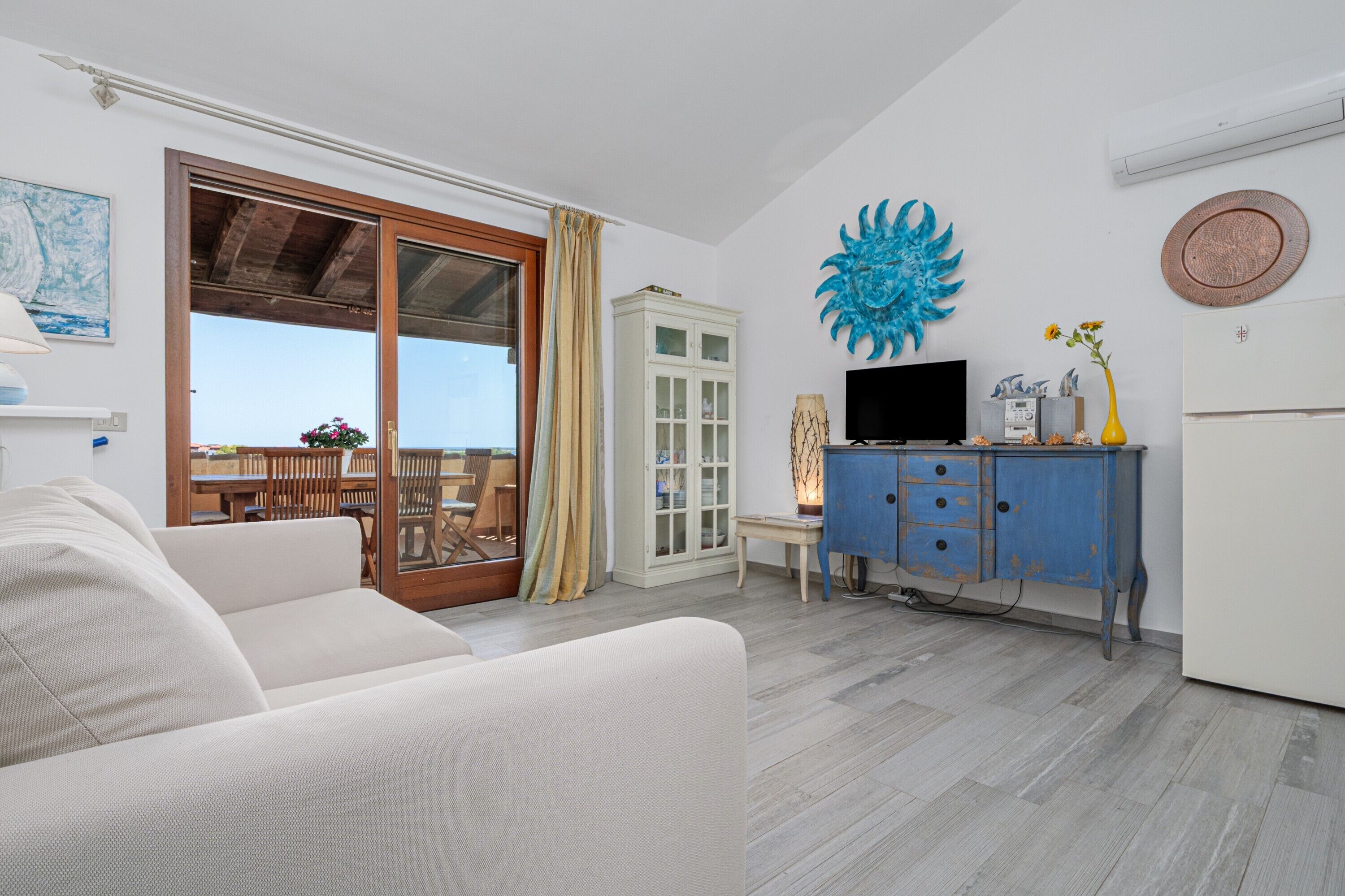 A living room with a sofa, a TV, a cabinet, and a view through a glass door.