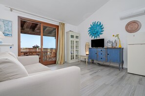 Un salón con sofá, televisor, mueble y vistas a través de un ventanal.