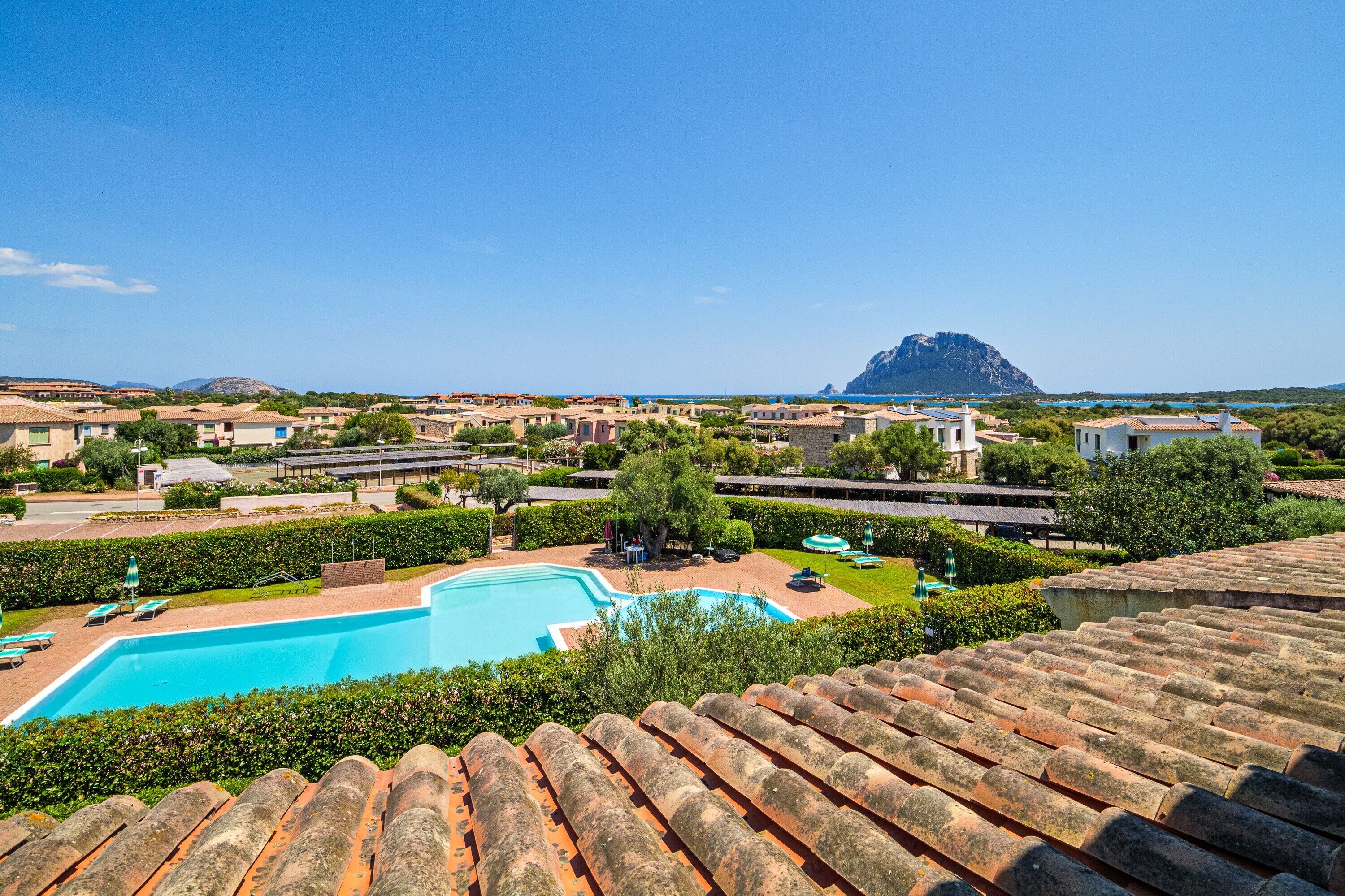 Ein Resort mit Schwimmbad, Gebäuden mit Terrakotta-Dächern und einem Berg im Hintergrund.