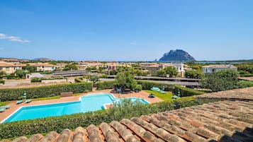 Ein Resort mit Schwimmbad, Gebäuden mit Terrakotta-Dächern und einem Berg im Hintergrund.
