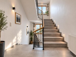 Eine Treppe mit hölzernem Geländer und schwarzen Metallspindeln, die zu einem Zwischenpodest mit einem Fenster und einem Blumentopf führt.