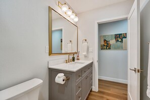 Une salle de bain avec un lavabo blanc, un grand miroir et un tableau accroché au mur.