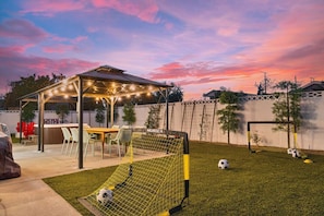 Ein Garten mit Fußballtor, überdachter Sitzgelegenheit und Grillplatz.