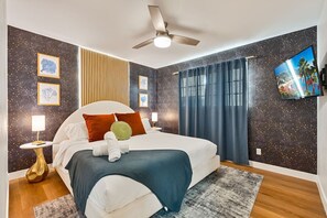 Ein Schlafzimmer mit Bett, Nachttischen, Deckenventilator und Fernseher an der Wand.