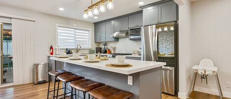 A modern kitchen with a central island, bar stools, stainless steel appliances, and a pendant light fixture.