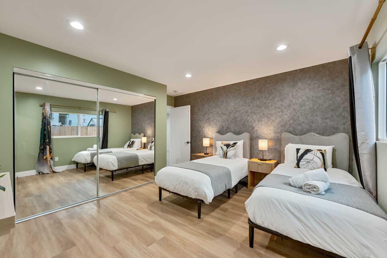 A hotel room with three beds, a large mirror, and a view of the outside.