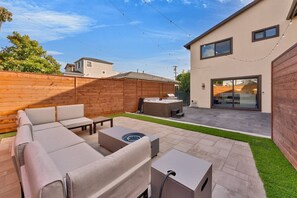 Ein Garten mit Terrasse, Gartenmöbeln, einem Whirlpool und einem modernen Haus.
