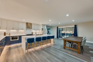 A modern kitchen with a central island, bar stools, and a dining table. - Modern 3BR Retreat | Hot Tub • BBQ • Pet-Friendly (San Diego)