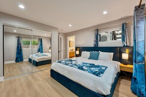 A bedroom with a large bed, a mirror, a wardrobe, and a bathroom visible through a glass door. - Modern 3BR Retreat | Hot Tub • BBQ • Pet-Friendly (San Diego)