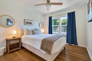 Ein Schlafzimmer mit Bett, Nachttischen, Deckenventilator und einem Fenster mit Vorhängen.