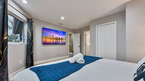 Una habitación de hotel con una cama, un cuadro de un paisaje urbano, una ventana con cortinas y una puerta.