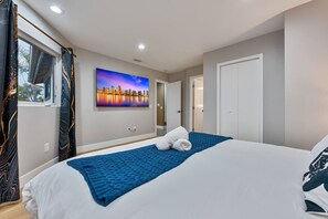 Ein Hotelzimmer mit einem Bett, einem Stadtbildgemälde, einem Fenster mit Vorhängen und einer Tür.