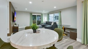 Una sala de estar moderna con una mesa redonda de mármol, un sofá gris y un televisor montado en la pared.