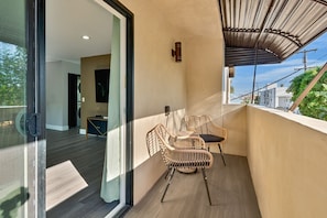 Ein Balkon mit Korbstühlen, einer Glastür zu einem Zimmer und Blick ins Freie.
