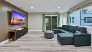 Una sala de estar moderna con un sofá modular, un televisor de pantalla plana, una mesa consola y un puerta corrediza de vidrio que da a un balcón.