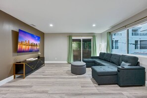 Ein modernes Wohnzimmer mit einer Eckcouch, einem Flachbildfernseher, einem Konsolentisch und einer Schiebetür zu einem Balkon.