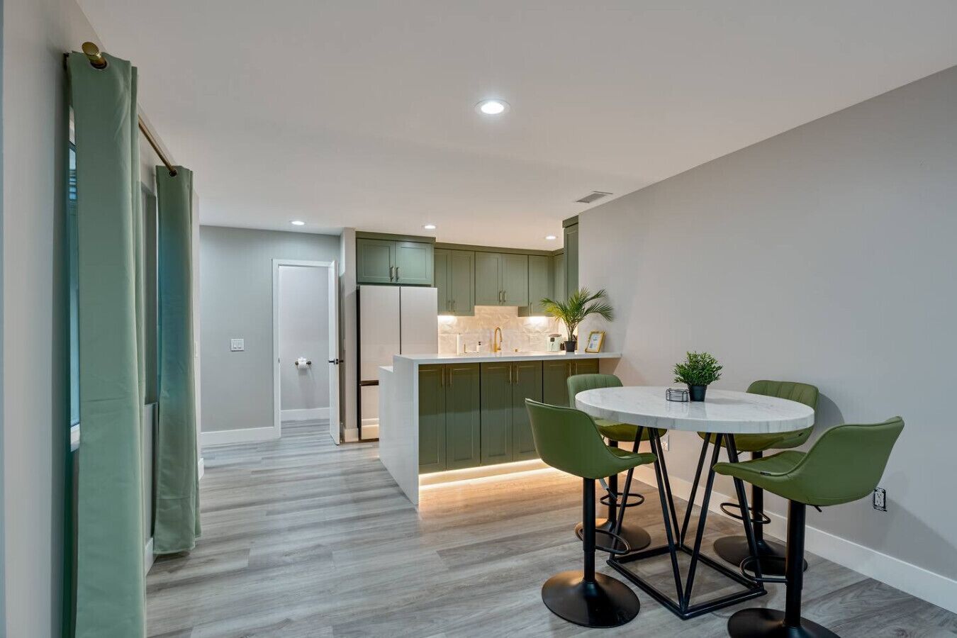 A modern kitchen with green cabinets, a white countertop, and a round dining table with green chairs.