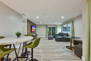 Ein modernes Wohnzimmer mit Essbereich, einer Sofagarnitur, einem an der Wand montierten Fernseher und einer Glastür zum Balkon.