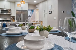 A modern kitchen with white cabinets, stainless steel appliances, and a dining area set with white plates, blue placemats, and glassware.