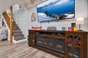 A modern living room with a fireplace, a television mounted on the wall, and a staircase. - Steps to Lake Tahoe | Fenced Yard | Modern Cabin (South Lake Tahoe)