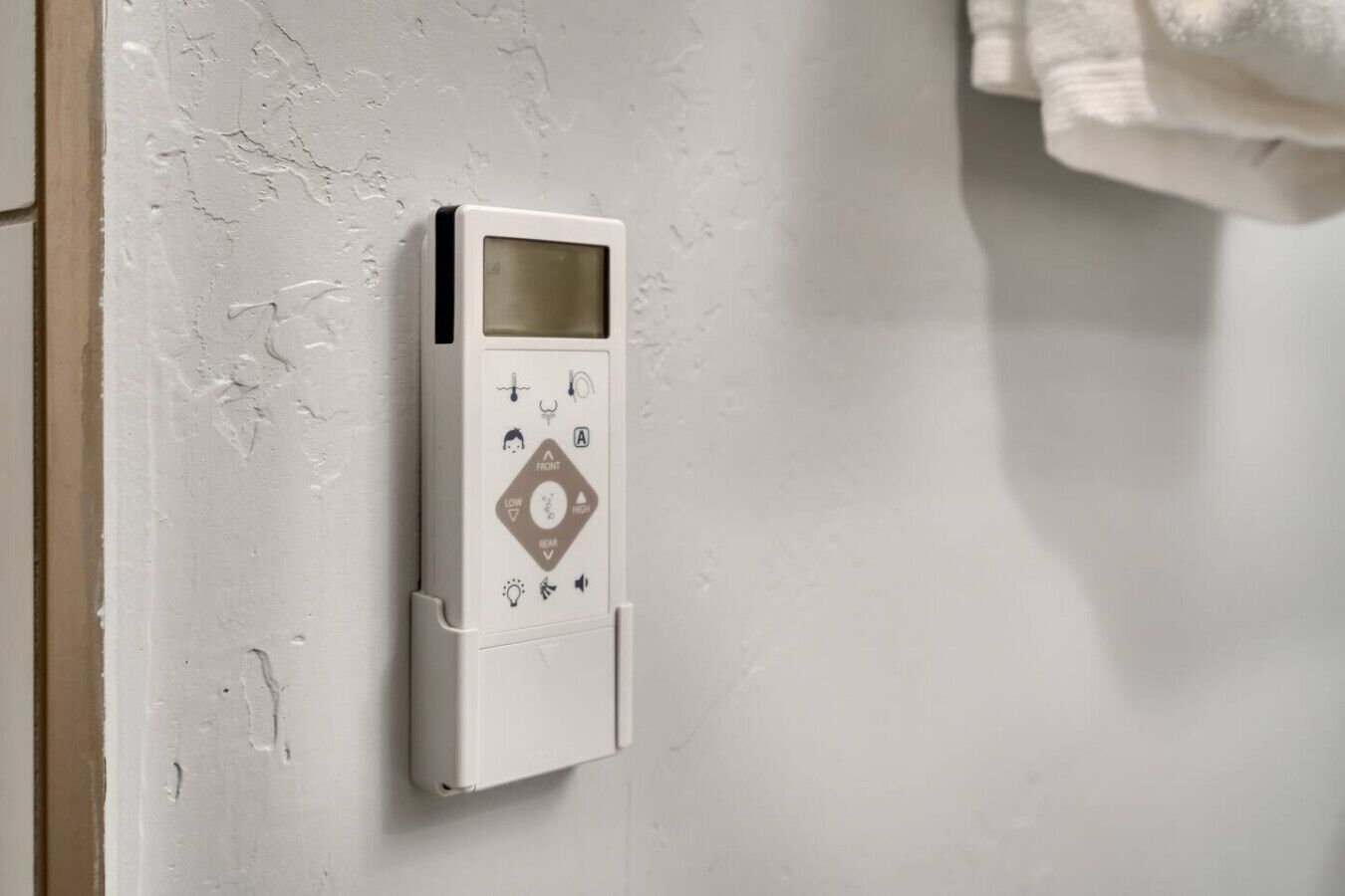 A thermostat mounted on a wall with a control panel featuring temperature adjustment and fan speed settings.