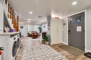 A laundry area with a washing machine, a sofa, and a dining area with a table and chairs. - Steps to Lake Tahoe | Fenced Yard | Modern Cabin (South Lake Tahoe)