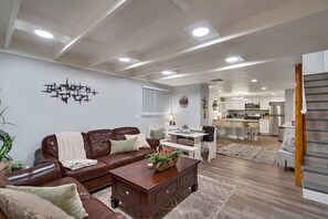 A modern living room with a brown leather sofa, a wooden coffee table, and a dining area with white chairs. - Steps to Lake Tahoe | Fenced Yard | Modern Cabin (South Lake Tahoe)
