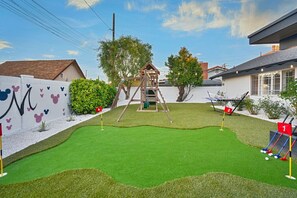Ein Garten mit Kunstrasen, einer Schaukel, einer Spielanlage und einem kleinen Poolbereich.
