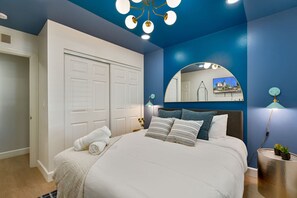Ein Schlafzimmer mit einem Bett, einem weißen Kleiderschrank, einem Spiegel und einer blauen Akzentwand.