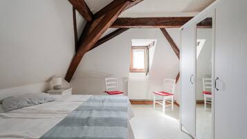 Une chambre à coucher comprenant un lit, deux chaises, une table de chevet, une fenêtre et une armoire.