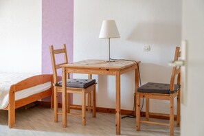 A room with a wooden bed, a small wooden table with a lamp, and two chairs. - Grand Gîte Le Bleuet "bi's anstetts" (Issenhausen)