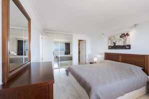 Habitació d'hotel amb un llit gran, un panell de fusta al capçal, un mirall, una tauleta de nit i una obra d'art penjada a la paret.