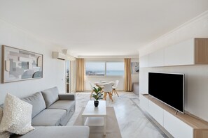 A modern living room with a sofa, coffee table, TV, dining area, and large windows with a view.
