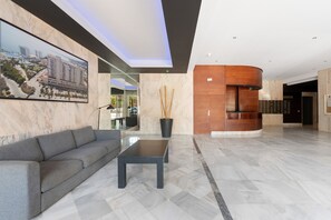 A modern lobby with a marble floor, a grey sofa, a black coffee table, and a reception desk with a wooden finish.