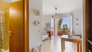 An open-plan living area with a wooden door, a white sofa, a dining table, and a view of the outdoors.