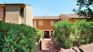 A pathway leading to a building with a tiled roof, surrounded by greenery.