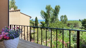 A balcony with a railing, a potted plant with flowers, and a view of a garden and distant landscape.