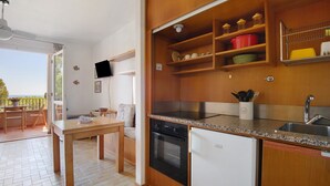 A kitchen with wooden cabinets, a stove, oven, and a refrigerator. There is a dining table with chairs and a TV mounted on the wall.