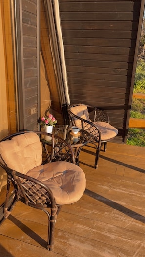 Una terraza de madera con sillas de mimbre y una mesa, una planta en maceta y una taza de café.