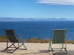 Zwei Strandstühle mit Blick auf die Küste, im Hintergrund Berge.