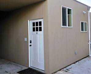 A single-story building with a white door marked with the number 2, a small window, and a security camera mounted on the wall. - Studio 2 - Comfortable Guest Studio by Cedars-Sinai, Beverly Hills (Beverly Hills)