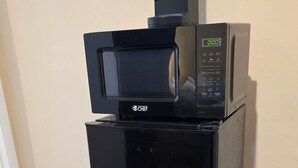 Eine schwarze gewerbliche Küche mit einer Mikrowelle, einer Kaffeemaschine und einem Mülleimer.