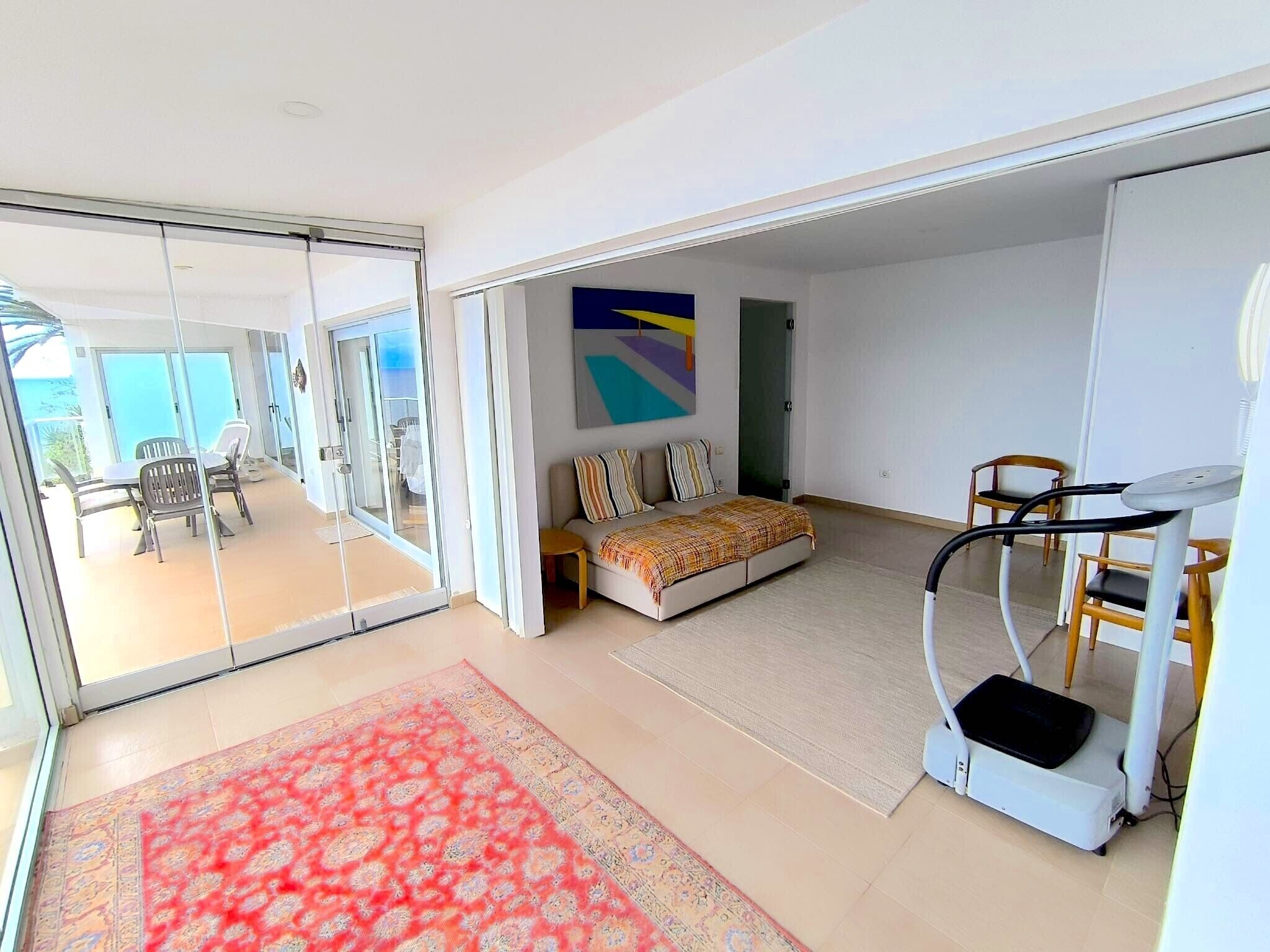 Un salon moderne avec un canapé, un tapis de course et une grande fenêtre donnant sur un balcon.