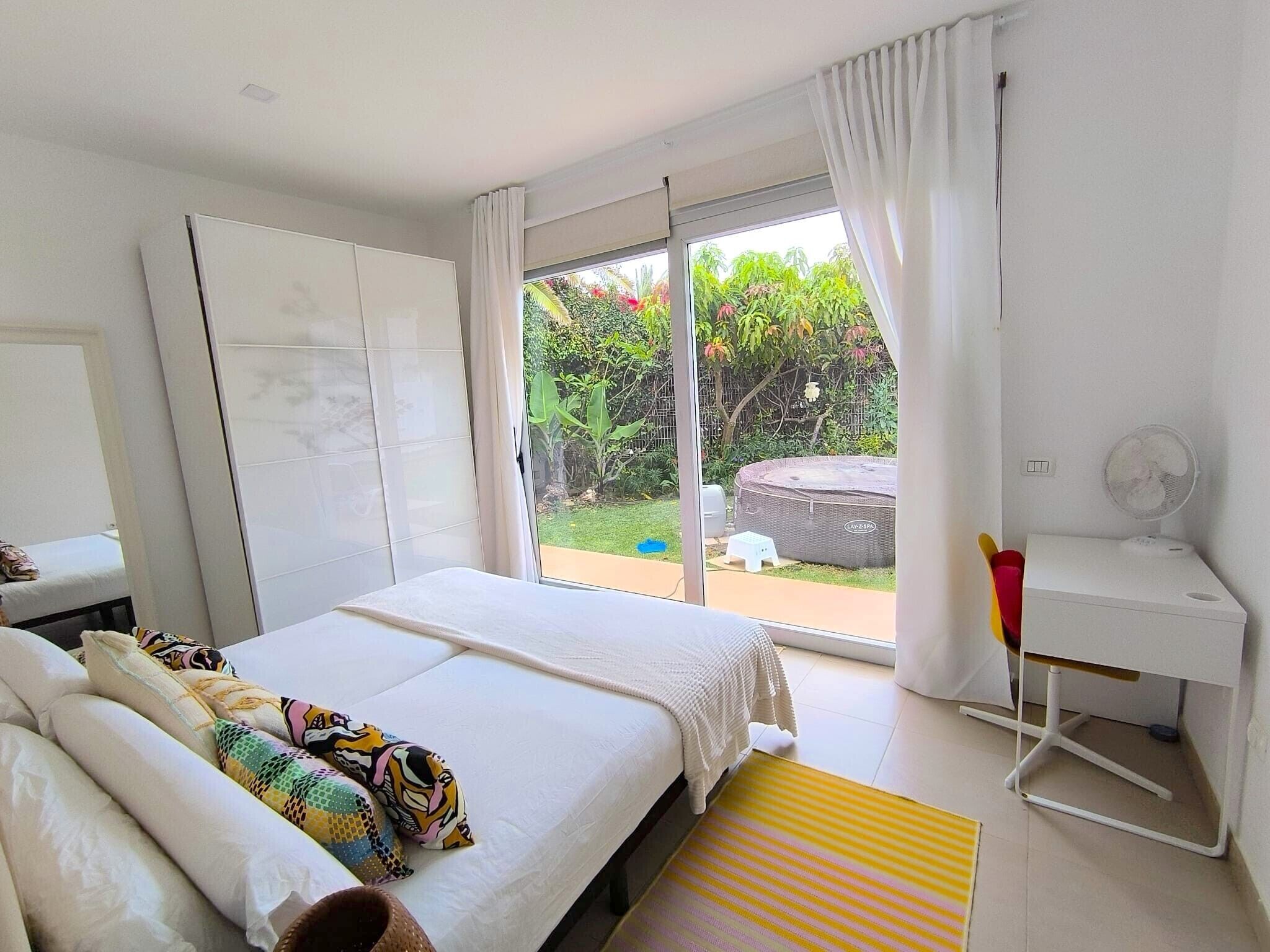Un dormitorio con cama, escritorio y vistas a un jardín a través de una puerta corrediza de vidrio.