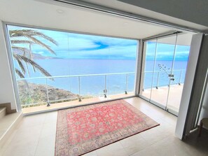 Una habitación con un gran ventanal que da a un balcón con vista al mar.