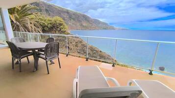 Ein Balkon mit Tisch und Stühlen, der auf eine Küstenlandschaft mit Blick auf das Meer und die Berge blickt.