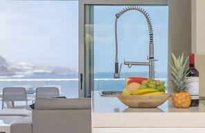 Cocina moderna con vista al océano, un bol de fruta en la encimera y una botella de vino.