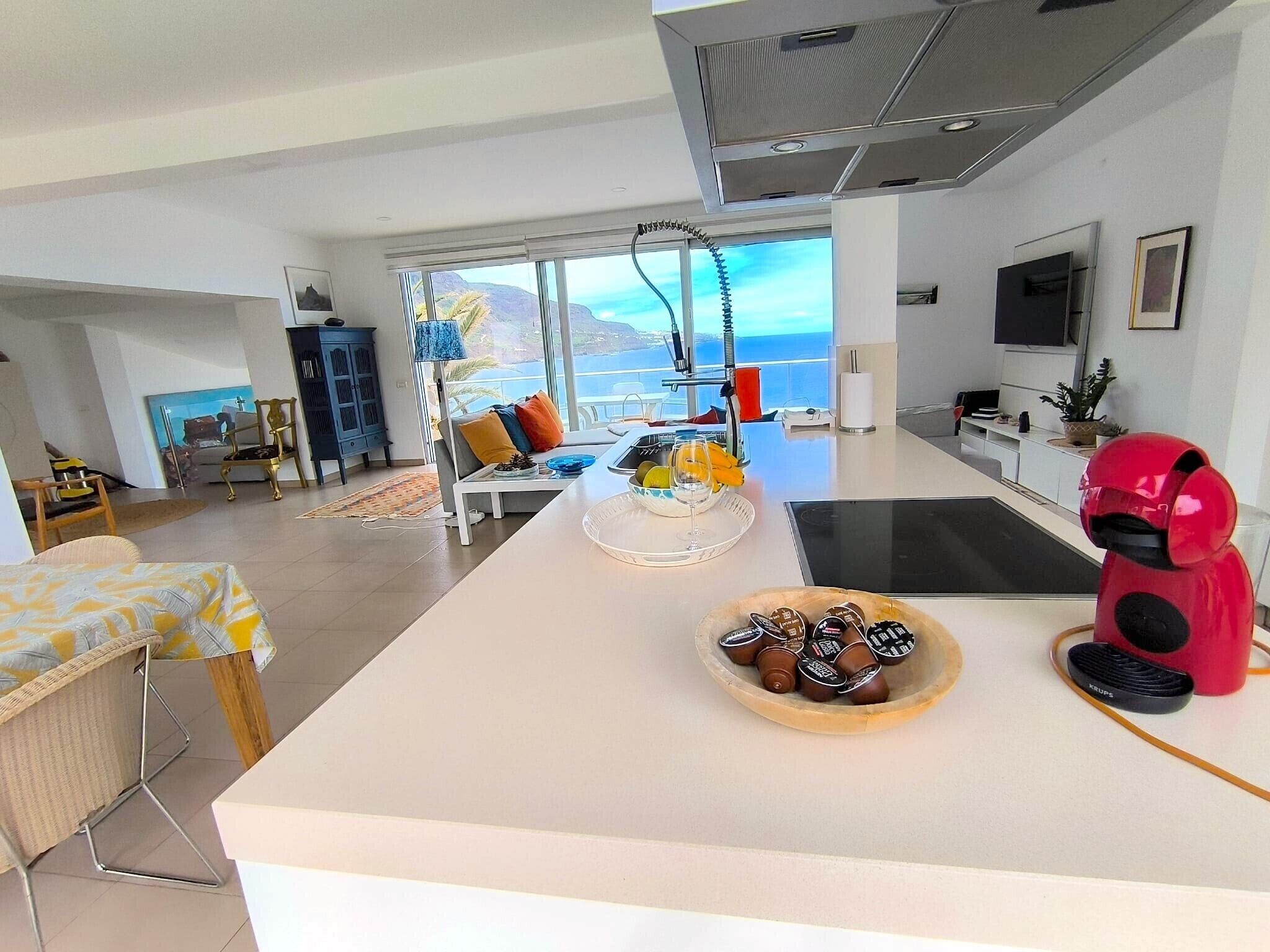 Una cocina moderna con una isla grande, un comedor con vistas y un espacio de sala de estar con televisor.