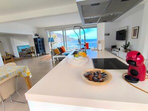 Une cuisine moderne dotée d’un grand îlot central, d’un coin repas offrant une vue agréable et d’un espace de vie avec un téléviseur.