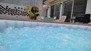 Un bain à remous extérieur offrant une vue dégagée sur la terrasse environnante, avec notamment des chaises longues et un mur décoratif.